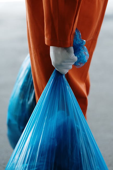A white plastic bin with the word 'waste' handwritten in blue ink on its side, placed on a white surface inside a room used for packing or sorting items during a house removal. The bin appears to be p